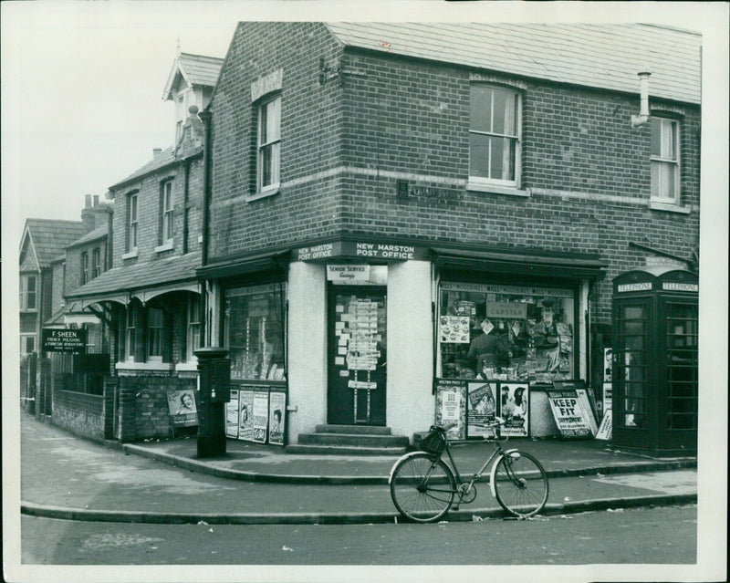 A man stands outside a post office in Madstone, England. - Vintage Photograph