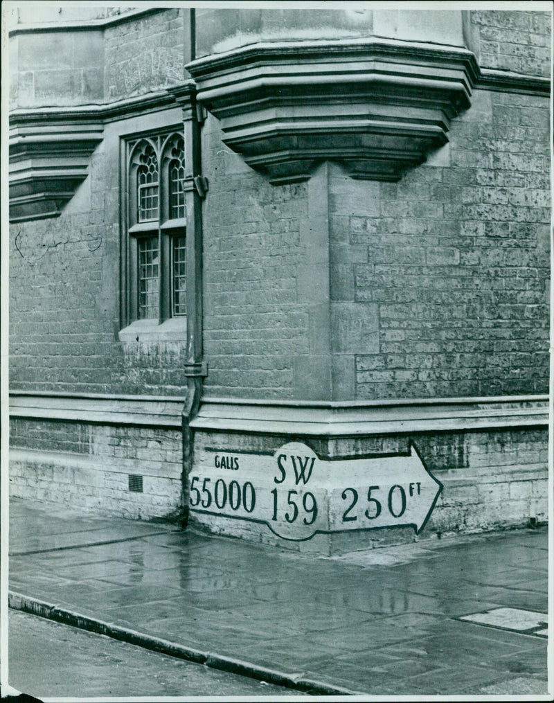 Chief Officer V. Fenn of the Oxford Fire Brigade inspects a war-time static water-tank sign on the corner of Brasenose College. - Vintage Photograph