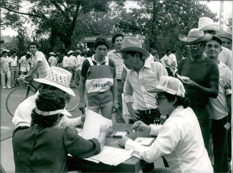 Voters in San Miguel, El Salvador line up to cast their ballots in the second round of elections in May 1984, supervised by a youthful "vigilante". - Vintage Photograph