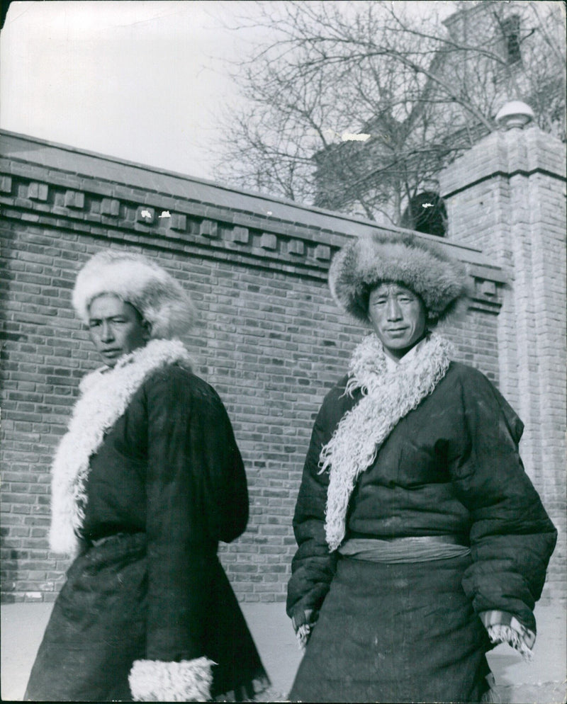 A woman is seen walking along a street in an urban area, carrying a large bag and a shopping cart. - Vintage Photograph