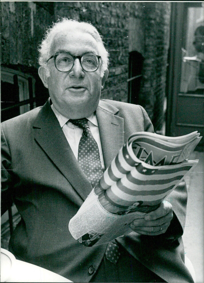 Henry Anatole Grunwald, Editor-in-Chief of "Time" magazine, poses for a photo with the "Time" magazine logo in the background. - Vintage Photograph