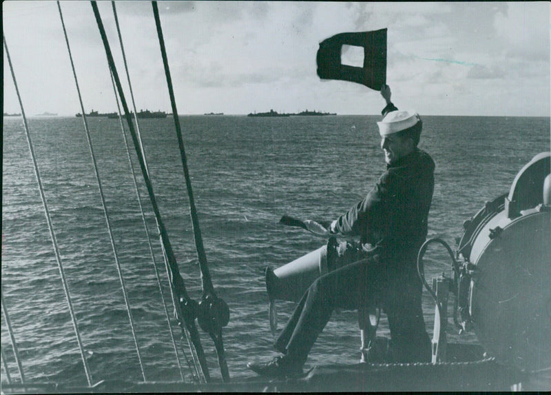 A signalman sends a message to other ships in an Allied convoy as it travels across the Atlantic. Flags and lights are often used for communication between ships in a convoy. - Vintage Photograph