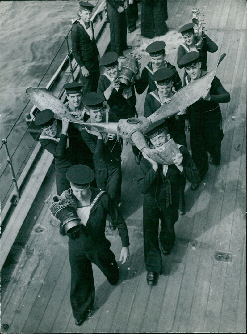 Members of the crew of H.M.A.S. Australia carry the remains of a Japanese suicide plane after surviving multiple attacks during the Battle of Luzon in 1945. - Vintage Photograph