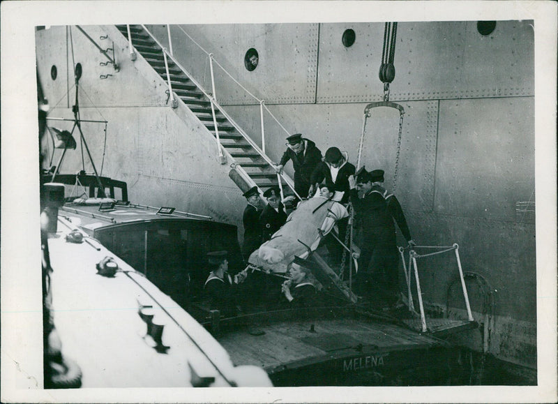 Medical personnel are seen carefully lowering a patient in a special stretcher into a waiting launch at the MELENA E 31 Hottan ship, on April 22, 1939. - Vintage Photograph