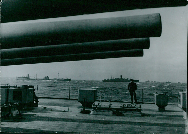 A British convoy on the Atlantic Ocean is seen from an accompanying warship, with the King George V in the foreground, in August 1941. - Vintage Photograph