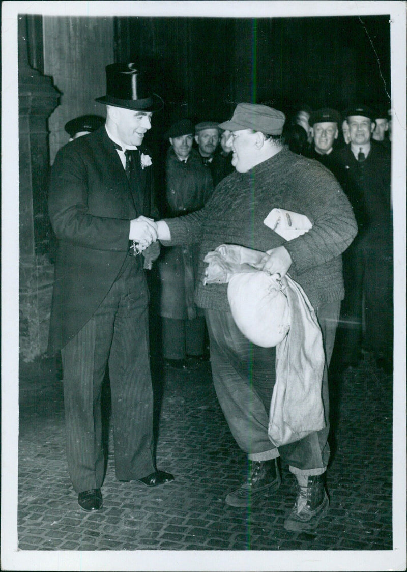 The crew of the British warship 'Hardy' arriving in London after surviving the Battle of the Fjords in 1940, with Chief Petty Officer G.W. Cook - the 'Heavyweight of the Navy' - shaking hands with an official in borrowed plumage. - Vintage Photograph