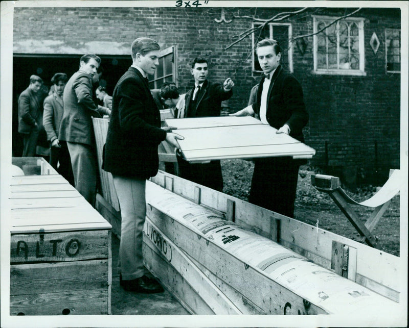 Members of the two crews in training reveal a boat wrapped in Italian newspapers. - Vintage Photograph