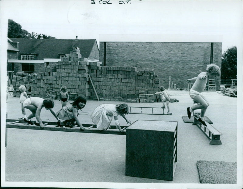 Students take a break from schoolwork to lean against a brick wall. - Vintage Photograph