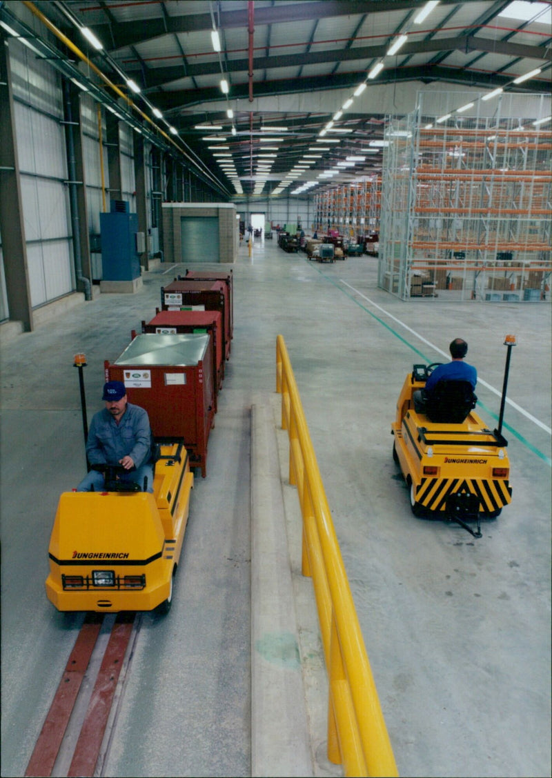 A worker stands in the middle of a warehouse filled with industrial equipment. - Vintage Photograph