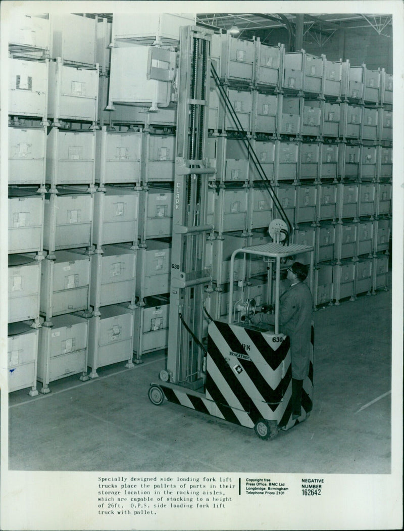 A specially designed side-loading forklift truck places pallets of parts into storage racks at a height of 26ft. - Vintage Photograph