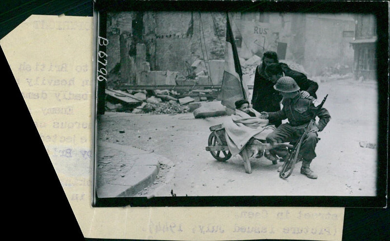 British and Canadian troops celebrate the taking of Caen, France on July 9th, 1944 in the aftermath of a fierce battle. An Artillery Soldier is seen here with a young French couple and their baby in the streets of the town. - Vintage Photograph