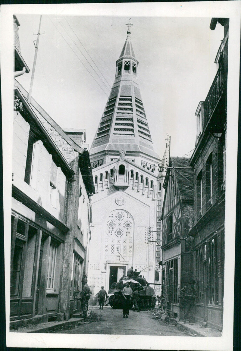 U.S. tank guards cross a street in Domfront, France, searching for snipers while a medium tank stands guard. - Vintage Photograph