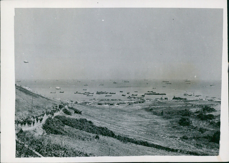 Allied troops and equipment move forward to their objectives on a beachhead in France, protected by naval gun fire and an air umbrella of Allied aircraft and barrage balloons. - Vintage Photograph