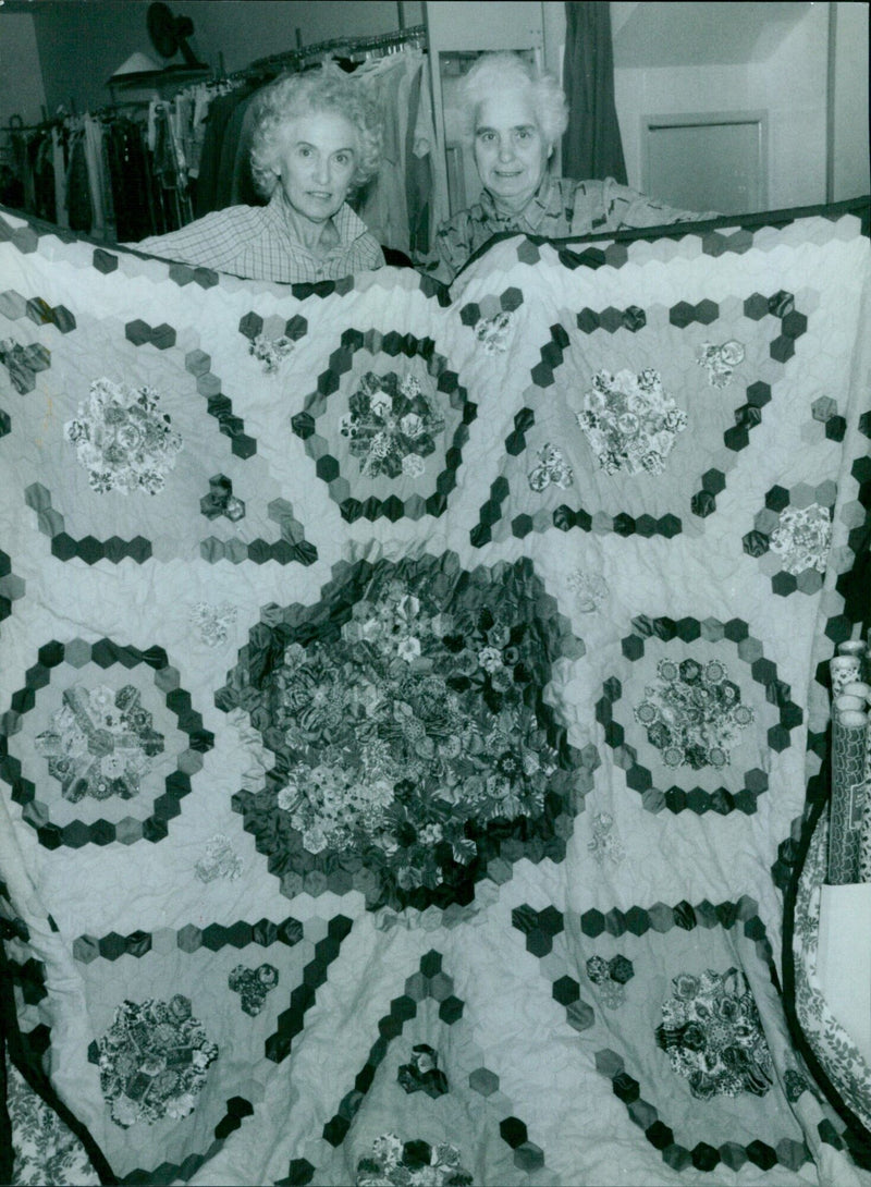 Helen Davray and Elizabeth Galpin holding a quilt at an Oxfam shop. - Vintage Photograph