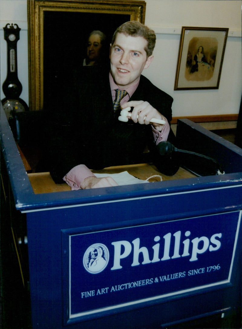 Auctioneer Rupert Fogden and porter John Durkin oversee antiques being sold at Phillips auction rooms in Oxford. - Vintage Photograph