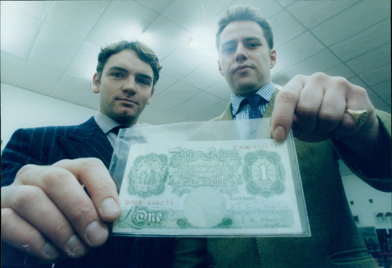 Roy Bolton and Peter Cullen of Phillips Auctioneers pose with an exotic painting, antiques, and an old one pound note. - Vintage Photograph