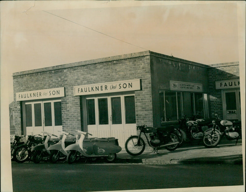 Two men stand inside the Faulkner Son & Son business, displaying a selection of British motorcycles, scooters, and mopeds. - Vintage Photograph