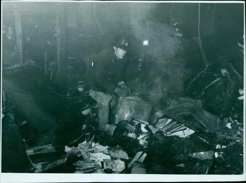 Firefighters clear smoldering debris at the scene of a fire. - Vintage Photograph