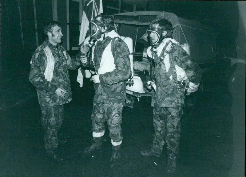 Firefighters donning breathing apparatus before entering a smoke-filled building. - Vintage Photograph