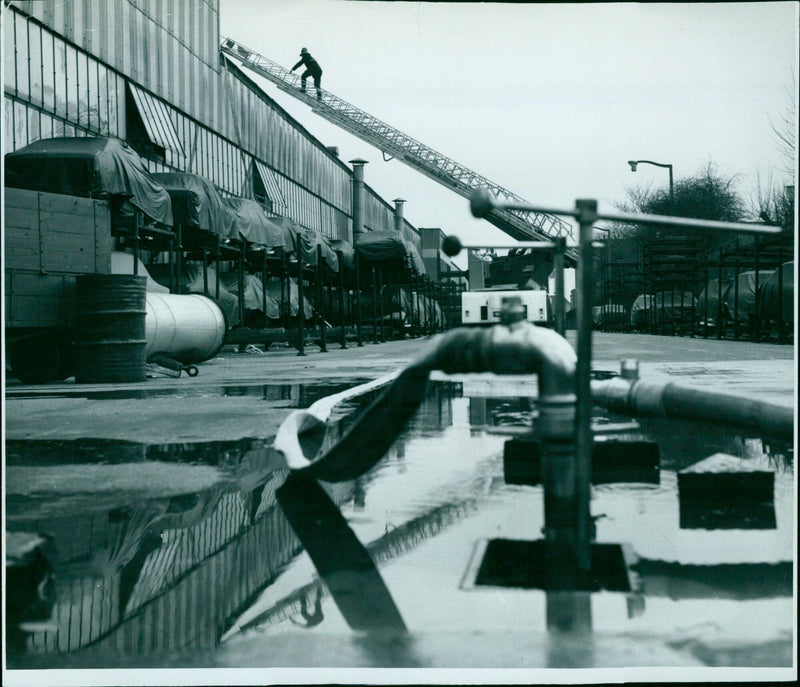 Fireman climbing up an extension ladder at a paint shop fire. - Vintage Photograph