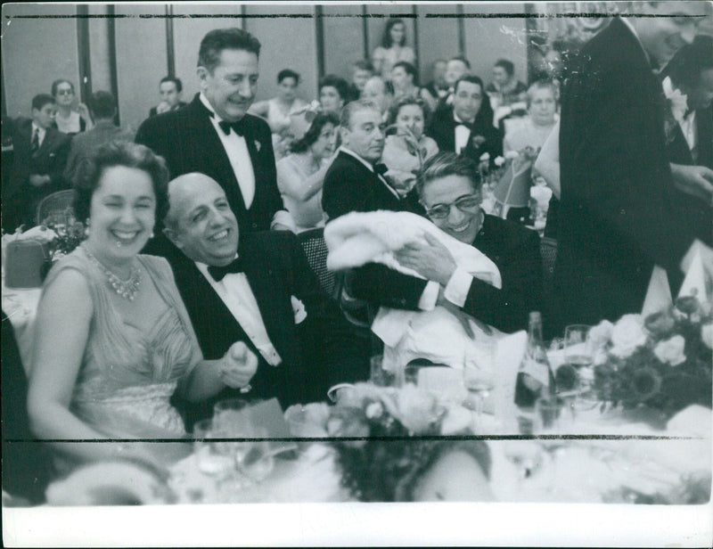 Comedian ONASSIS entertained the party guests by wearing funny paper hats and making faces. - Vintage Photograph