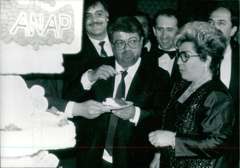 TURGUT & SEMRA OZAL OPS Turkish Prime Minister Turgut Ozal and his wife, Semra, sampling a cake baked to commemorate the third anniversary of the founding of Ozal's Homeland Party. - Vintage Photograph