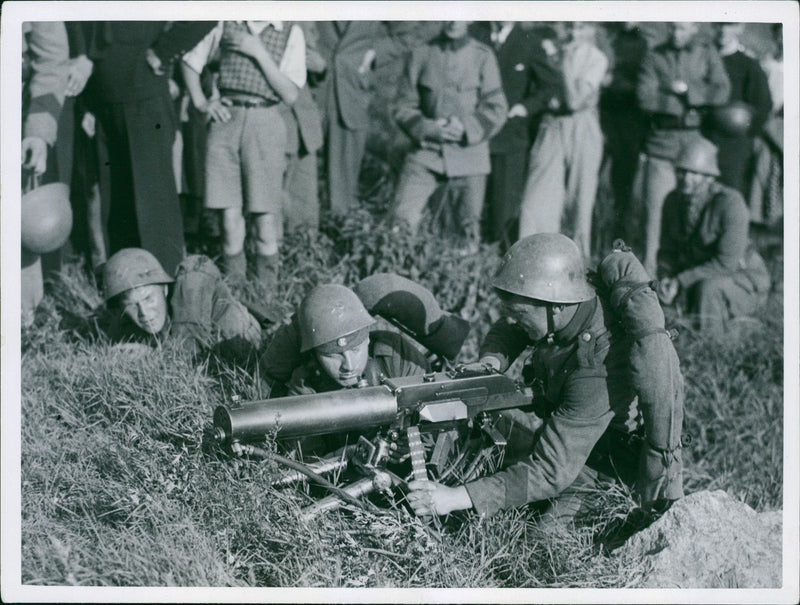 Soldiers using machine gun, other people standing around looking at them. - Vintage Photograph