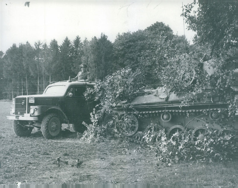 Generel Nils Swedlund seen standing through the roof of a truck passing a leafy tank during his inspection - Vintage Photograph