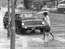 A woman with an umbrella crossing at the pedestrian crossing during heavy rain.woman, crossing, road, holding, umbrella, rainy, day. - Vintage Photograph