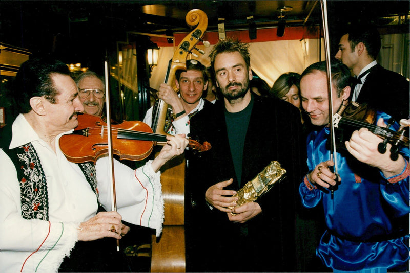 Regisseur Luc Vesson is proud of his award while a quartet musician is playing around him. - Vintage Photograph