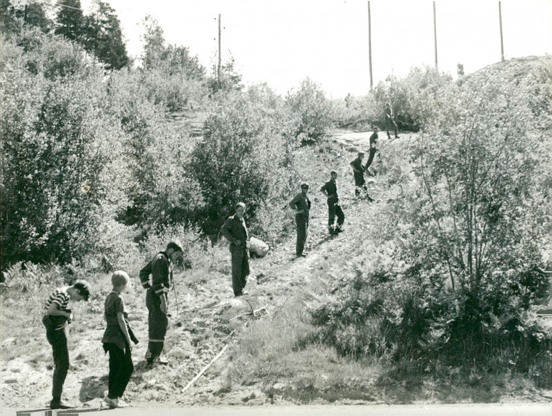 Police officers and interested civil combing the area in search of clues that could be linked to the murder. - Vintage Photograph