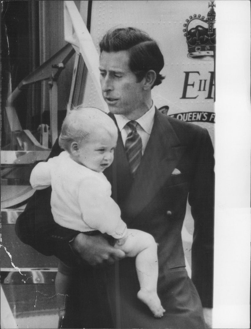 Prince Charles carries on his son, Prince William. They are at the airport in Aberdeen and head to Balmoral, Scotland, for a summer break. - Vintage Photograph