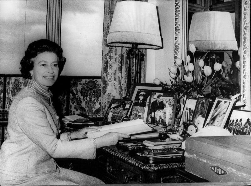 Queen Elizabeth II sits at her desk and goes through old photographs. - Vintage Photograph