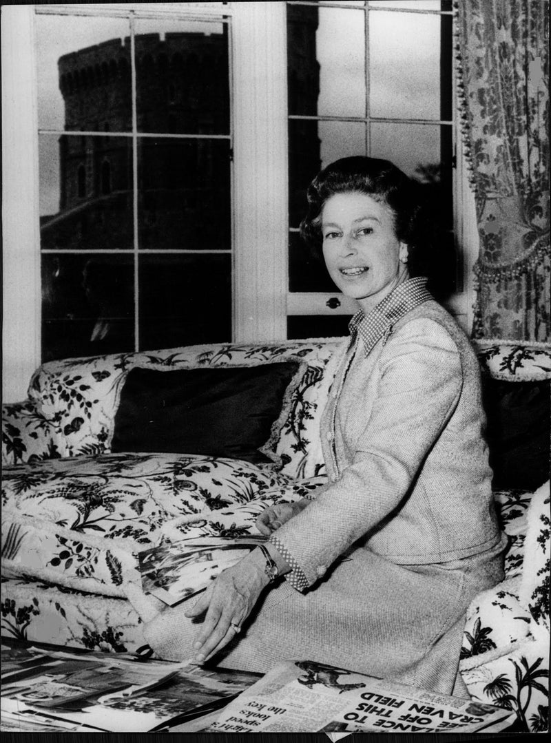 Queen Elizabeth II sits on the couch and goes through the old newspaper she saved. - Vintage Photograph