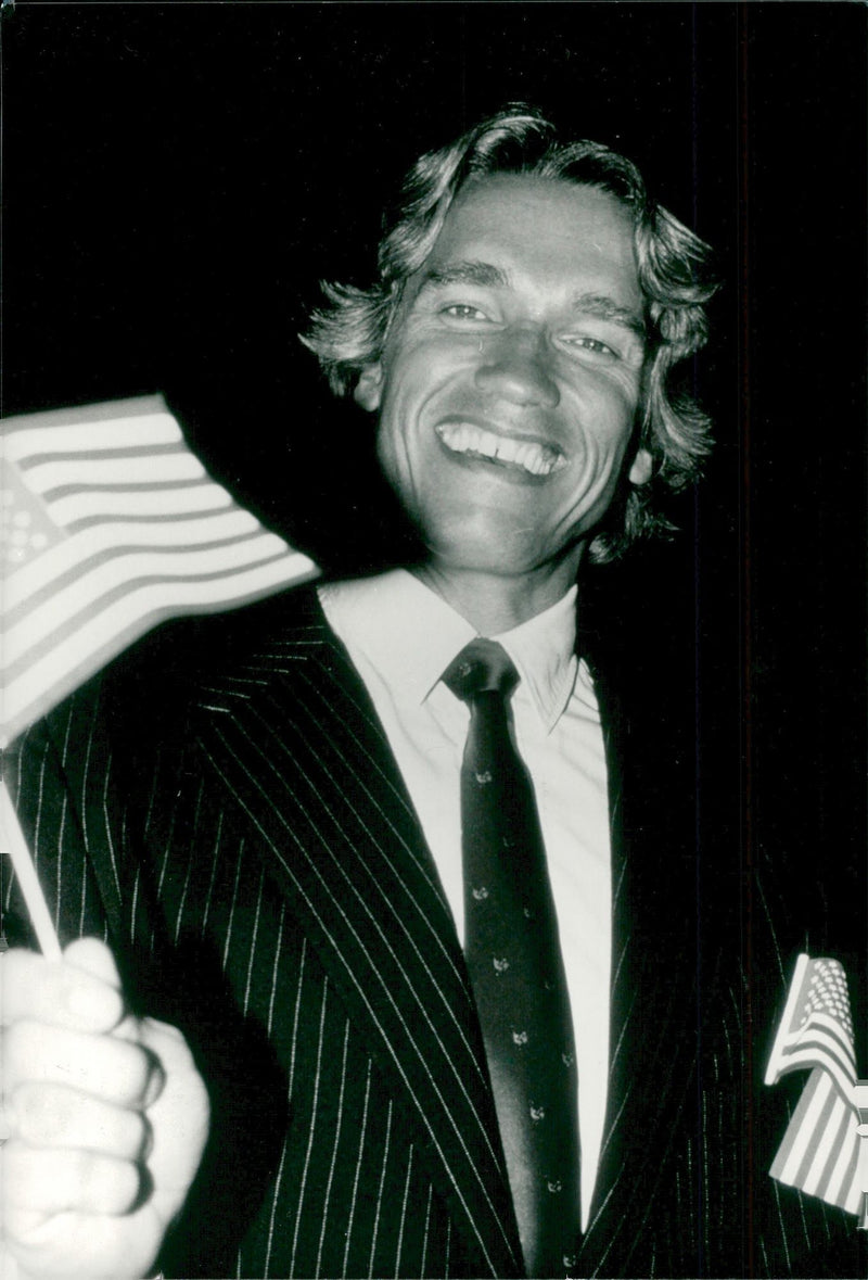 Actor Arnold Schwarzenegger blows smoothly with a flag after being assigned his American citizenship - Vintage Photograph